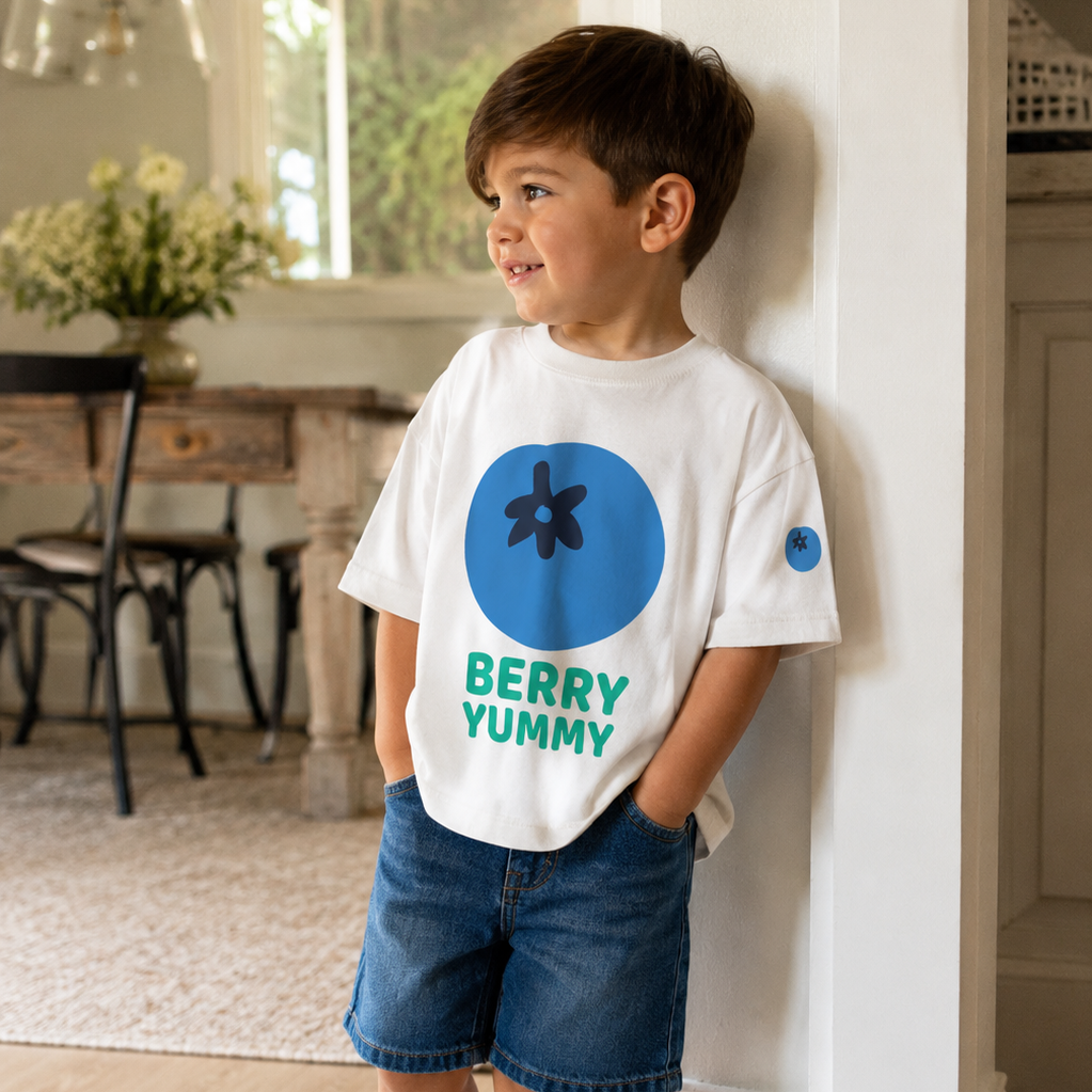 Child wearing a white t-shirt with blue and green design, standing indoors.