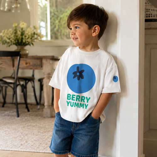 Child wearing a white t-shirt with blue and green design, standing indoors.